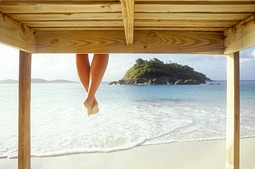 United States, Virgin Islands, St. John, Legs of woman sitting on wooden pier above sea