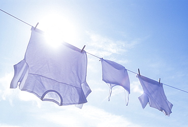 Low angle view of laundry drying on clothesline against sky and sun