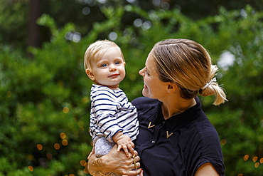 Mother holding baby girl, outdoors, smiling