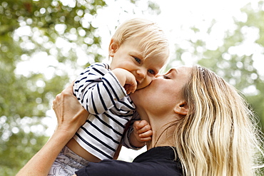 Mother kissing baby girl on cheek, outdoors