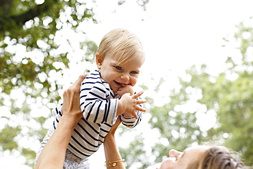 Mother holding baby girl in air, smiling