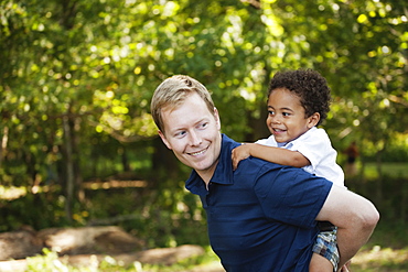 Side view of father giving son a piggyback smiling