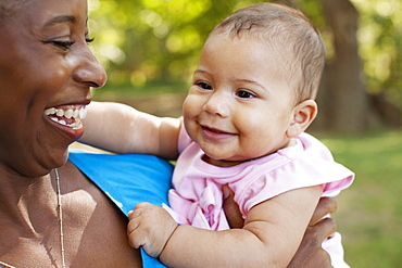 Head and shoulders of mother holding baby girl looking away smiling