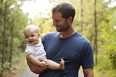 Happy mid adult man carrying baby daughter on forest track