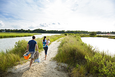 Rear view of mid adult parents carrying baby daughter on riverside picnic