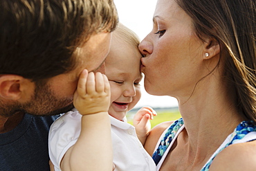 Close up of mid adult parents kissing baby daughter