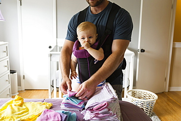 Mid adult man doing chores with baby daughter in baby sling