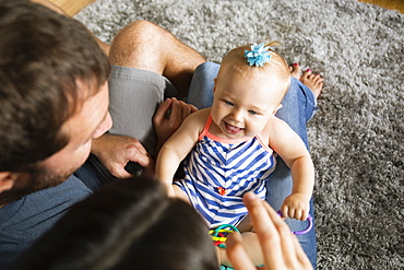 High angle view of mid adult couple playing with baby daughter on lap