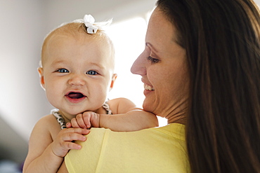 Over the shoulder portrait view of happy baby girl and mid adult mother