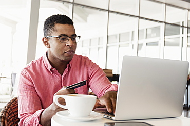 Young man in coffee shop, using laptop, holding credit card