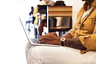 Young man in coffee shop, using laptop, mid section