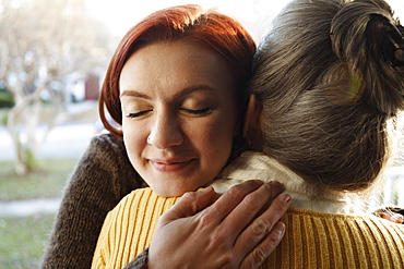 Close up of senior woman and adult daughter hugging on porch