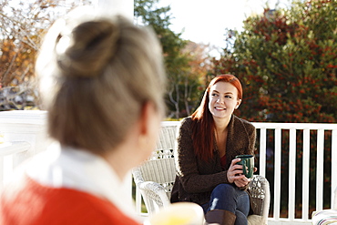 Senior woman and adult daughter chatting and drinking coffee on porch