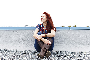 Portrait of young woman, sitting on rooftop, wearing earphones