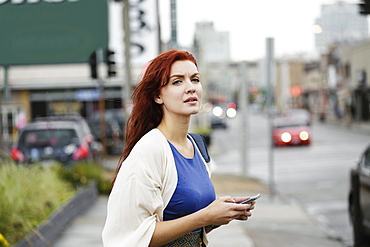 Young woman with long red hair, using smartphone in street