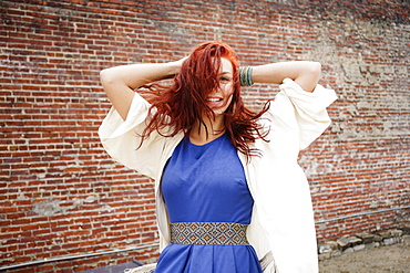 Young woman with long red hair, hands behind head, smiling