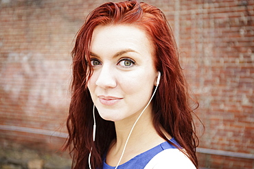 Portrait of young woman with long red hair, wearing earphones, close-up