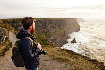 Mid adult man on The Cliffs of Moher with camera, The Burren, County Clare, Ireland