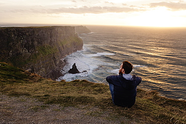 Mid adult man sitting on The Cliffs of Moher, The Burren, County Clare, Ireland