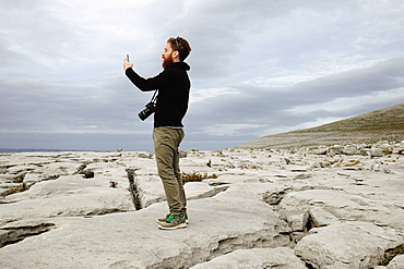 Mid adult man taking photo on phone, The Burren, County Clare, Ireland