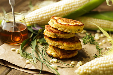 Stack of corn fritters with honey and corn cobs on kitchen table