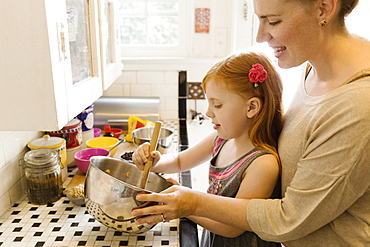 Girl and mother mixing ingredients in bowl in kitchen