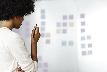 Young woman holding pen, looking at adhesive notes