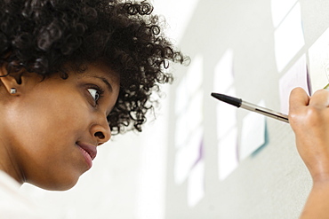 Young woman writing on adhesive note