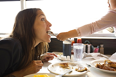 Toddler daughter feeding mother from fork in diner