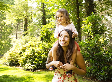 Mother giving toddler daughter a shoulder carry in park