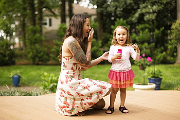 Mother and toddler daughter blowing bubbles in garden