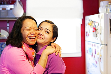 Portrait of mother hugging daughter in kitchen