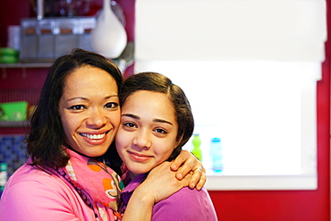 Portrait of mother hugging daughter in kitchen
