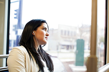 Young woman traveling on light train wearing earphones