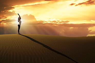 Dubai, United Arab Emirates, Woman practicing yoga on sand dune in desert at sunset