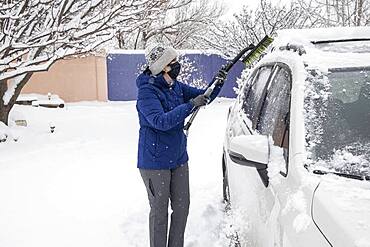 USA, New Mexico, Santa Fe, Woman in face mask removing snow from car