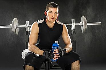 Muscular man training with barbell and holding water bottle