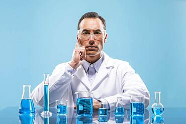 Portrait of scientist with beakers with blue liquid in foreground