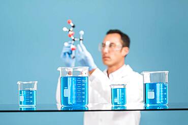 Scientist holding molecule model, blue liquid in beakers in foreground