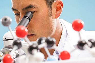 Close-up of scientist looking through microscope, molecular model in foreground