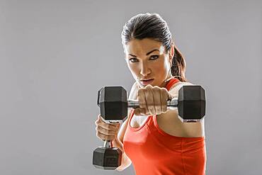 Studio portrait of athletic woman in red sleeveless top exercising with dumbbells