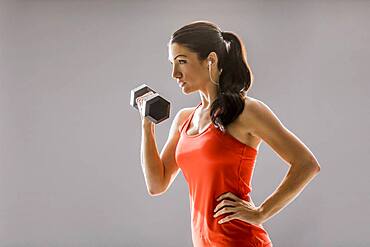 Studio shot of athletic woman in red sleeveless top exercising with dumbbell