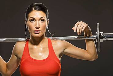 Studio portrait of athletic woman in red sleeveless top with barbell