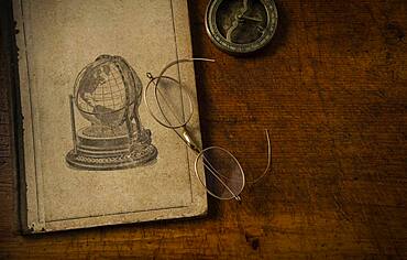 Old book resting on old wooden desk top with old eyeglasses and small sundial