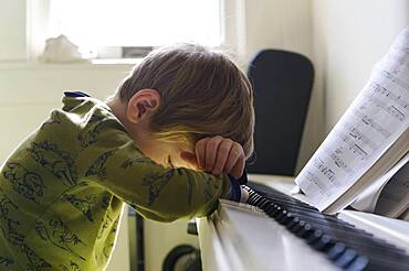 Sad boy (6-7) leaning on piano