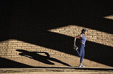 Woman stretching near brick wall in sunlight