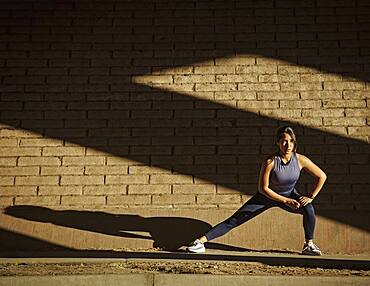 Woman stretching near brick wall in sunlight