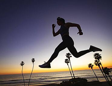 Silhouette of woman jumping on beach at sunset