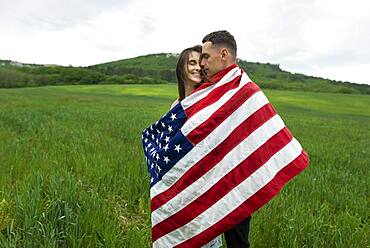 Young couple wrapped in American flag in wheat field