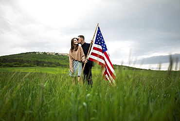 Young couple with American flag kissing in wheat field